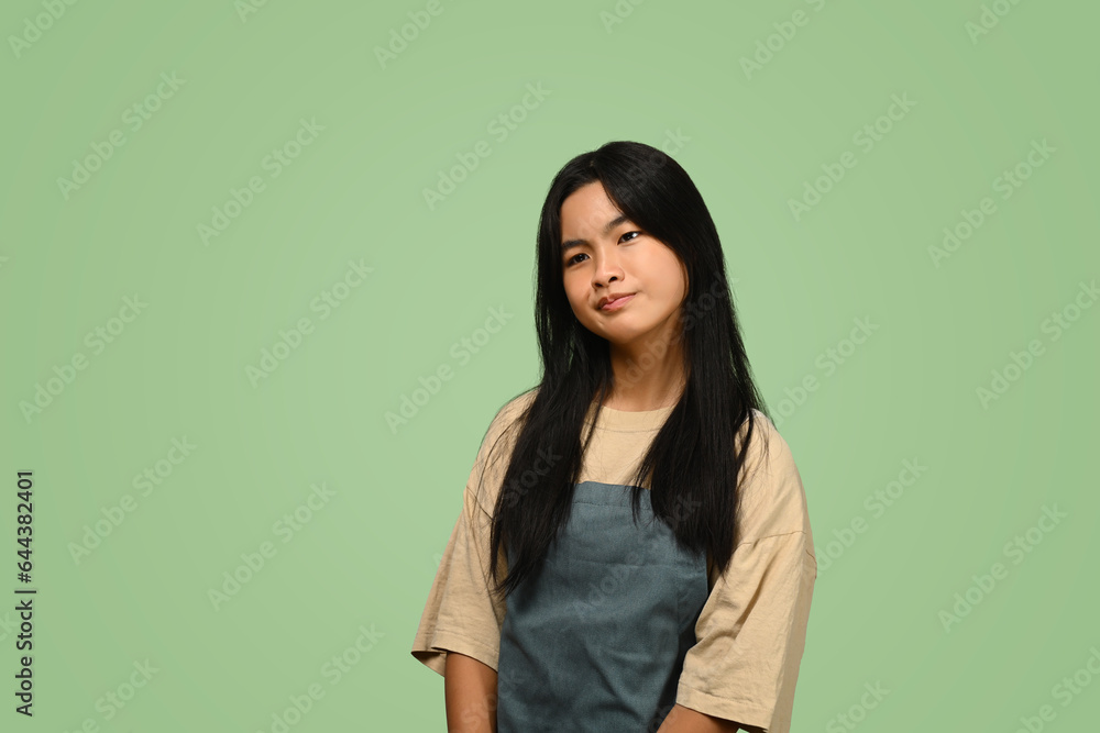 Asian teenage girl wearing apron standing against on green background Asian teenage girl wearing apron standing against on green background