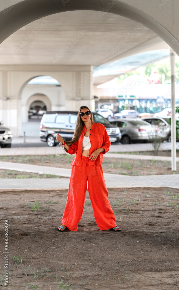 Obraz premium Summer portrait of a girl with long blond hair. A girl in orange clothes and sunglasses stands on the street.