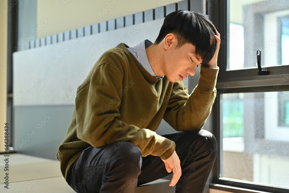 Unhappy young man holding his head, suffering from depression. Loneliness, depression, mental heath concept Unhappy young man holding his head, suffering from depression. Loneliness, depression, mental heath concept