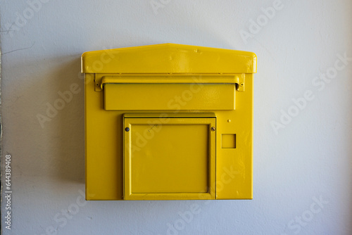An old yellow letter box on a white wall