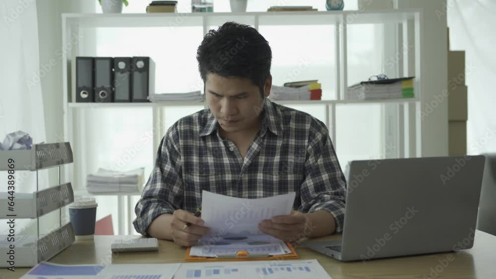 Young asian businessman working at home calculating financial graph data on laptop and checking with finance documents investment and business strategy and summarized in chart Young asian businessman working at home calculating financial graph data on laptop and checking with finance documents investment and business strategy and summarized in chart