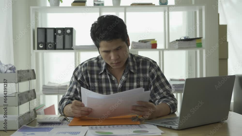 Stressed young Asian man managing financial bills and credit cards, calculating taxes, financial debt at home, husband planning household expenses and business planning. Stressed young Asian man managing financial bills and credit cards, calculating taxes, financial debt at home, husband planning household expenses and business planning.