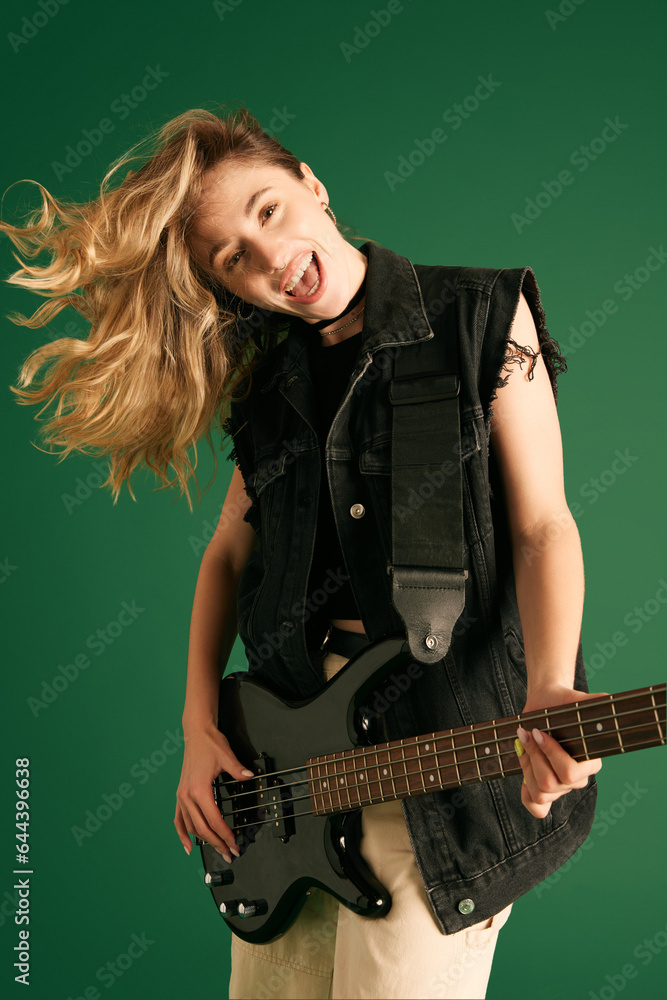 Portrait of young girl, musician in stylish clothes, making performance, playing electric guitar against green studio background. Concept of music, human emotions, youth, fashion, lifestyle, ad