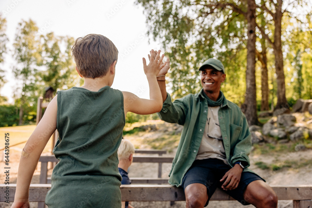 Rear view of boy giving high-five to male camp counselor during summer camp Rear view of boy giving high-five to male camp counselor during summer camp