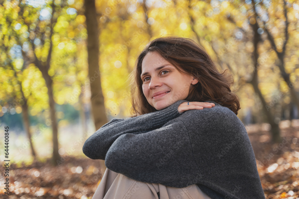 Portrait of young woman in a sweater enjoying the beauty of nature and the sun sitting in the autumn park Portrait of young woman in a sweater enjoying the beauty of nature and the sun sitting in the autumn park