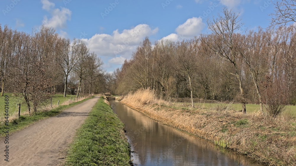 Hiking trail along a draining channel in nature on a sunny spring day in Schoonaarde, Flanders, Belgium