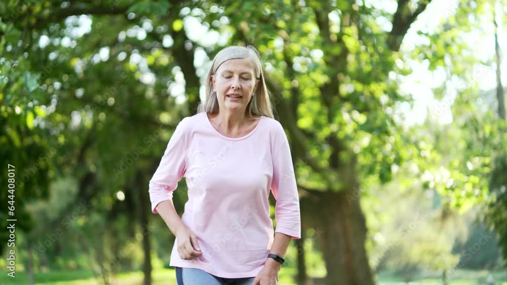 Senior active gray haired woman is short of breath during a morning run in city park. Mature old fitness female leans on her knees, wipes the sweat from her forehead with her hand and breathes deeply Senior active gray haired woman is short of breath during a morning run in city park. Mature old fitness female leans on her knees, wipes the sweat from her forehead with her hand and breathes deeply