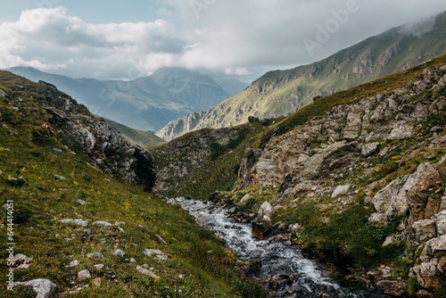 Stream on a mountain background. Green mountains covered with clouds. View of mountain river in summer