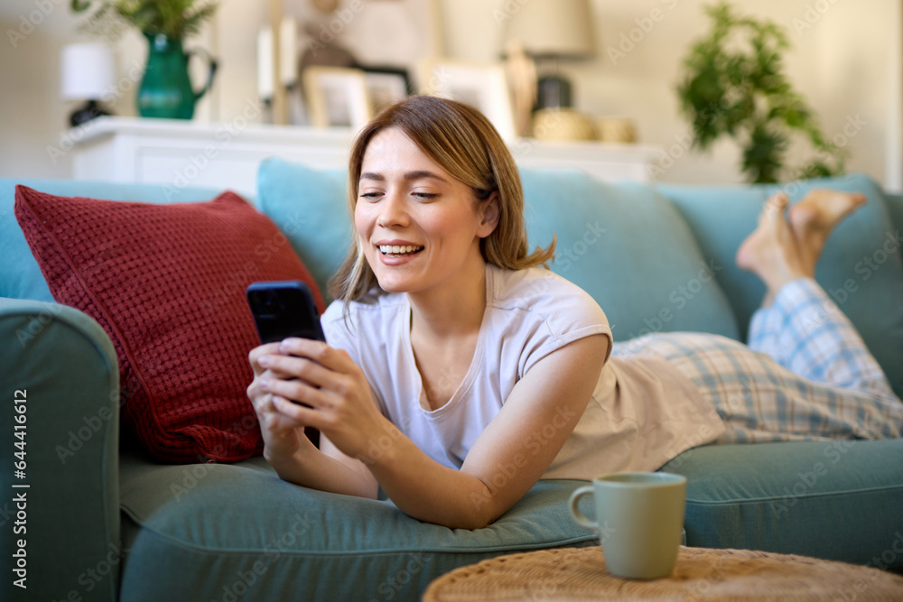 Happy woman text messaging on mobile phone while relaxing in the living room Happy woman text messaging on mobile phone while relaxing in the living room