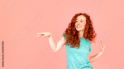 Portrait of a happy woman with long red hair dancing in green t-shirt on pink background Lifstyle concept