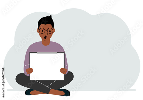 A man sits crossing his legs and holds a clipboard with a white read sheet for the text in his hands.