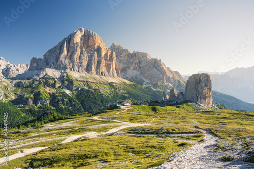 Cinque Torri peaks and Tofane Mountains at summer cloudless morning with green grass lighteen by warm light of sun from right side and path inf front photo