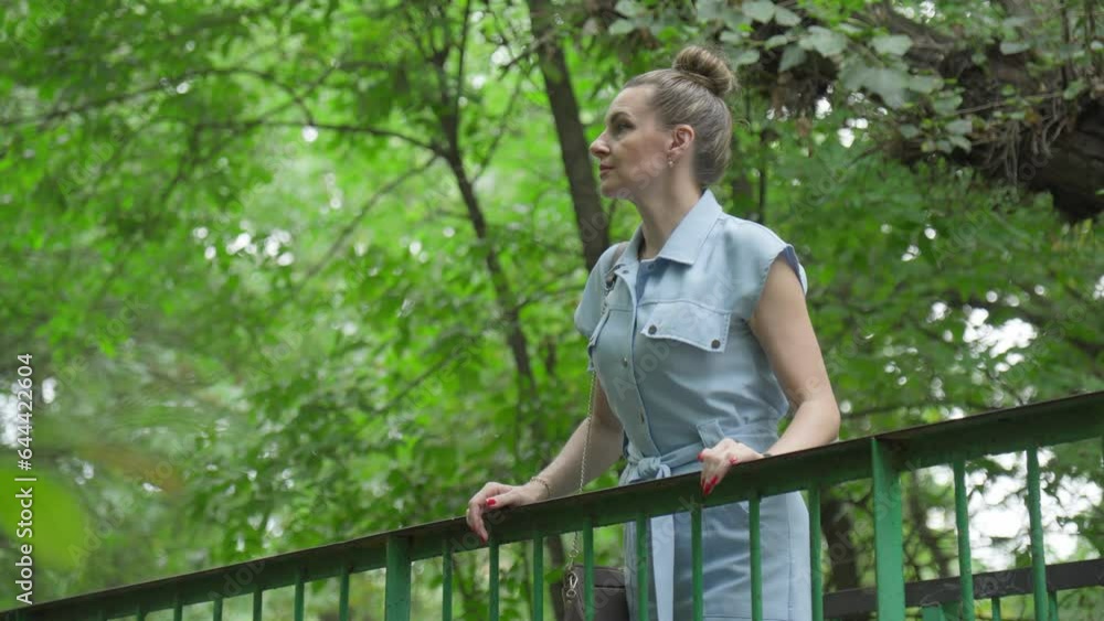 Middle-aged woman is bored alone in park leaning on handrail of bridge. Middle-aged woman is bored alone in park leaning on handrail of bridge.
