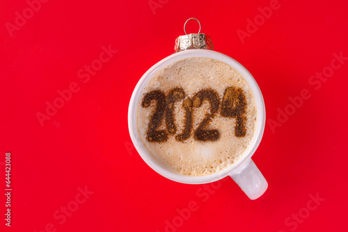 New year Christmas flat lay with festive decorated coffee or hot chocolate with latte art drawing 2024. Holiday hot drink mug as Christmas tree ball, with ornaments, decor on red background top view