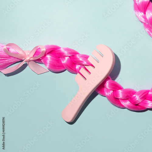 Shiny pink hair braided and decorated with satin bow and wooden comb, hair care minimal creative concept.