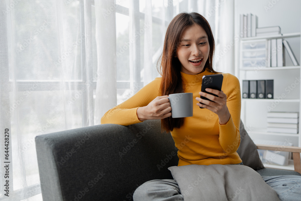 Asian woman is in the living room and uses social media on a smartphone. Female company employee on vacation. Using vacation time and free time to relax at home. Weekend vacation day doing activities. Asian woman is in the living room and uses social media on a smartphone. Female company employee on vacation. Using vacation time and free time to relax at home. Weekend vacation day doing activities.