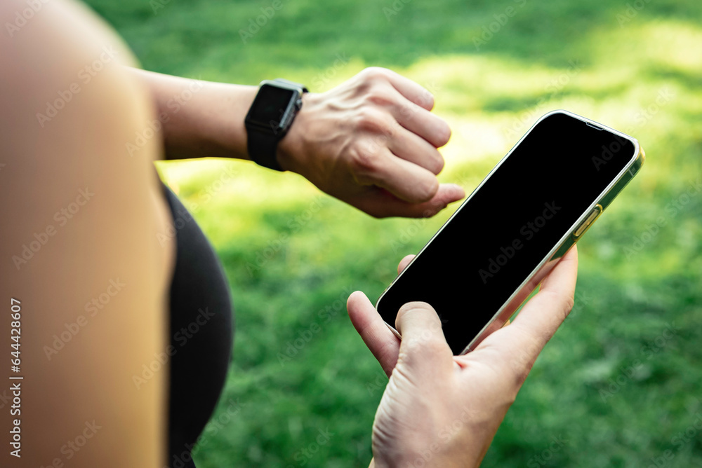Close up of athlete holds a mobile phone in his hands and tracks the results of training on a smartwatch.