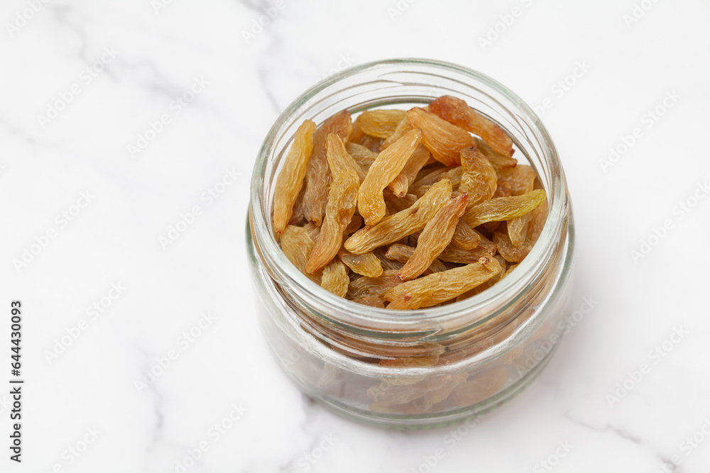 Fresh golden long-size raisins (dry grapes) into a glass jar isolated on marble background. Top view. Fresh golden long-size raisins (dry grapes) into a glass jar isolated on marble background. Top view.