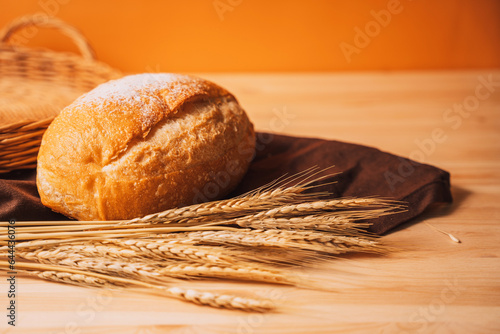 Freshly baked loaf of bread next to ears of wheat on a wooden table.