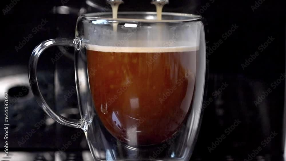 A modern coffee machine pours delicious coffee into a transparent cup standing on a metal support, close-up. Coffee. A modern coffee machine pours delicious coffee into a transparent cup standing on a metal support, close-up. Coffee.