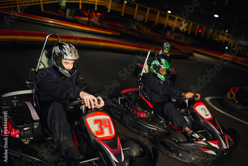 focused multicultural racers driving go kart cart on indoor circuit, speed racing and motorsport