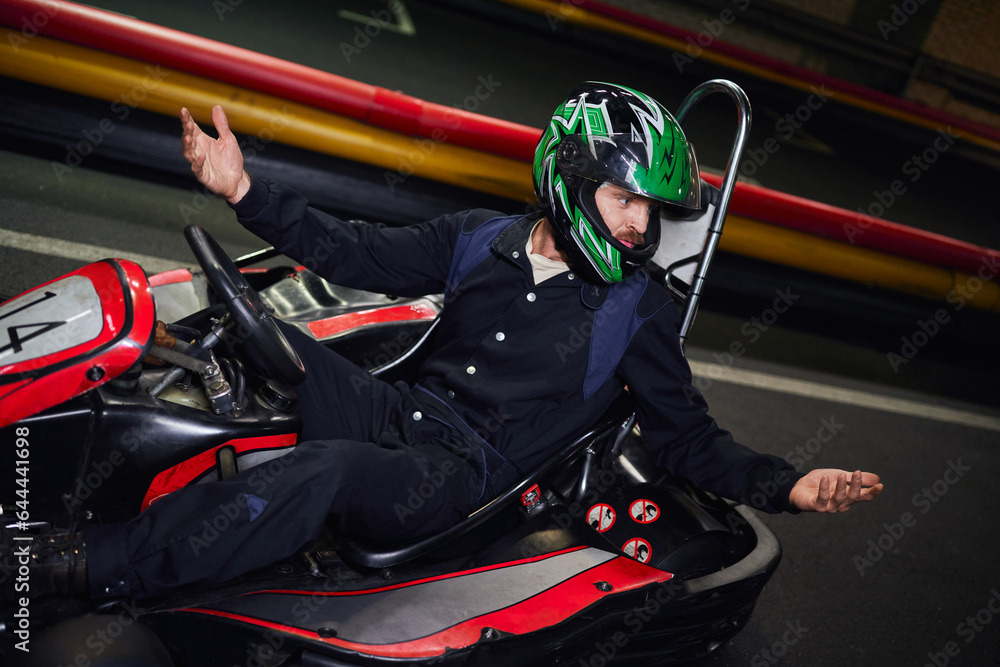emotional driver in helmet gesturing while driving sport car for karting on indoor circuit