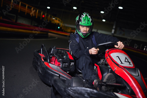 emotional racer in helmet and sportswear driving go kart on indoor circuit, adrenaline concept