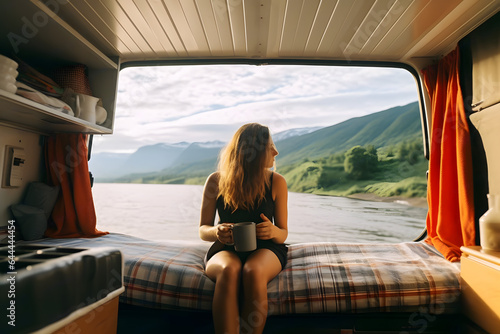 Camper girl holding coffee cup inside camper van at riverside.