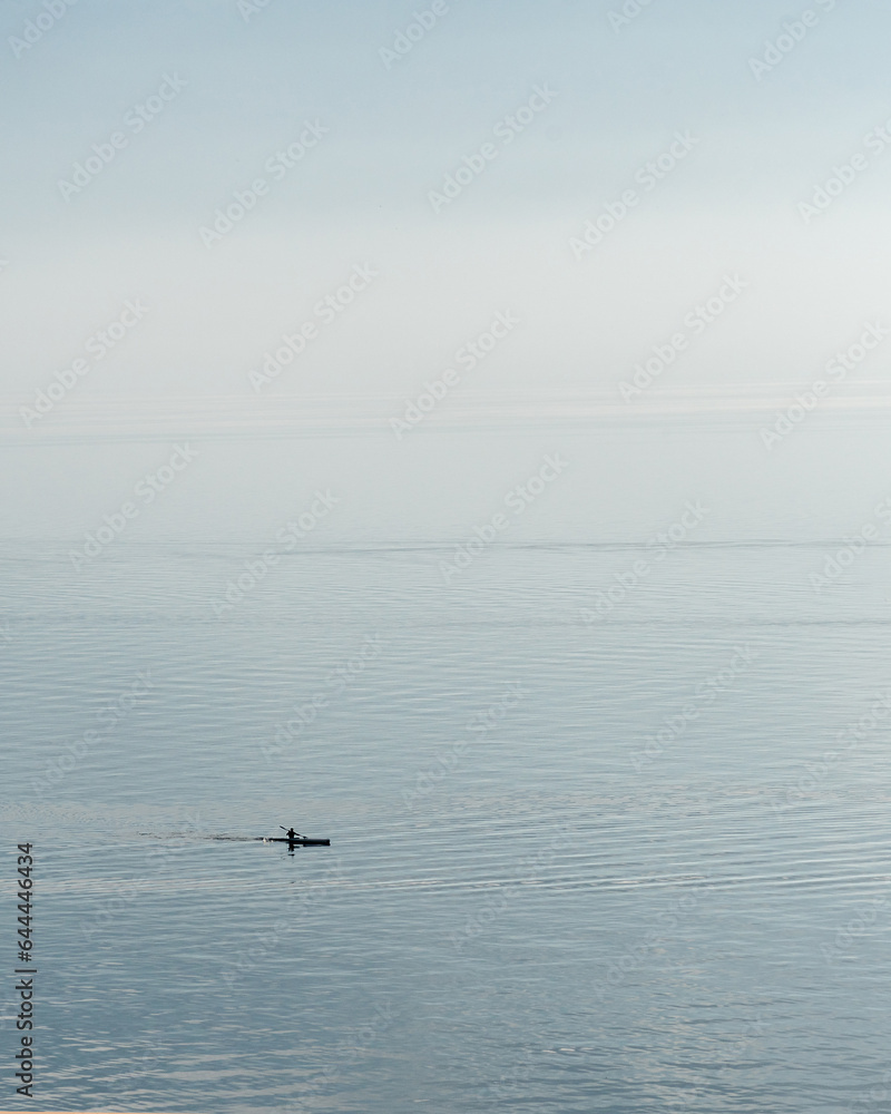 View of a person paddling a kayak on an outdoor lake on a foggy day.