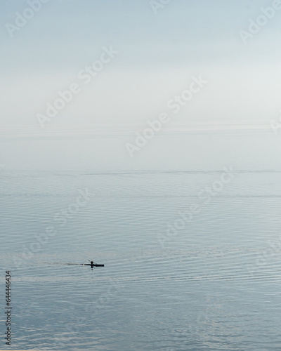 View of a person paddling a kayak on an outdoor lake on a foggy day. © fotosdanielgbueno
