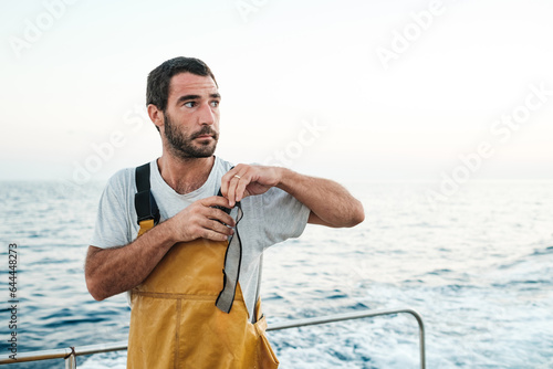 Confident young ethnic fisherman tightening braces of bib on sailboat photo