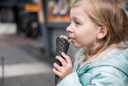 Little girl child in a jacket eats ice cream on the street