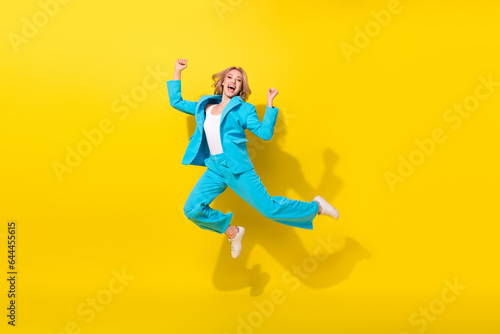 Full size photo of overjoyed good mood girl dressed blue jacket trousers jumping raising fists win gambling isolated on yellow background