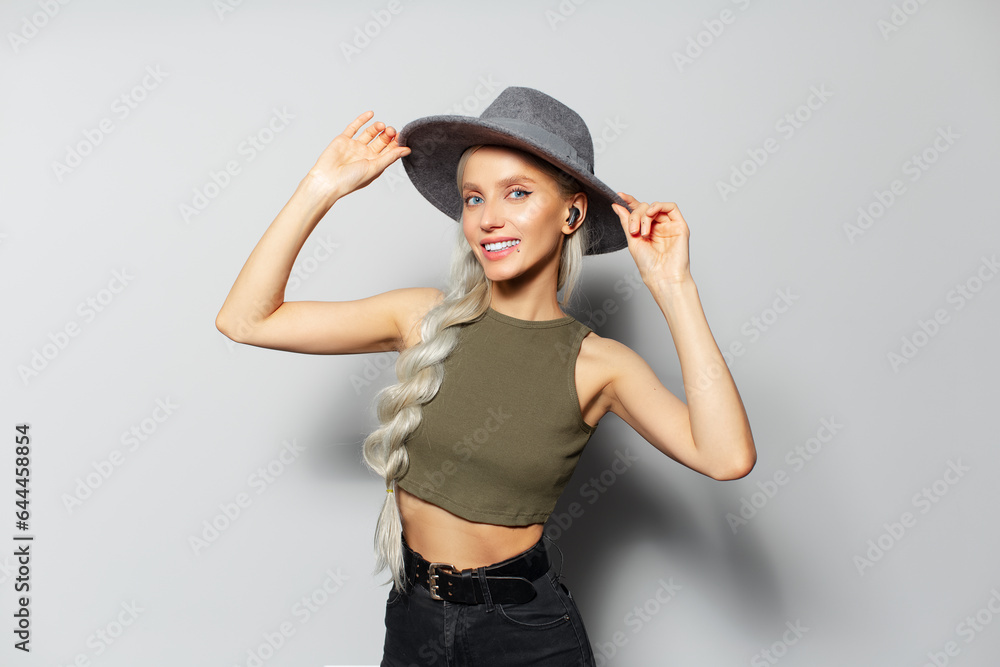 Studio portrait of attractive happy blonde girl with wireless earbuds in ears, on white background. Wearing grey hat and green shirt. Studio portrait of attractive happy blonde girl with wireless earbuds in ears, on white background. Wearing grey hat and green shirt.