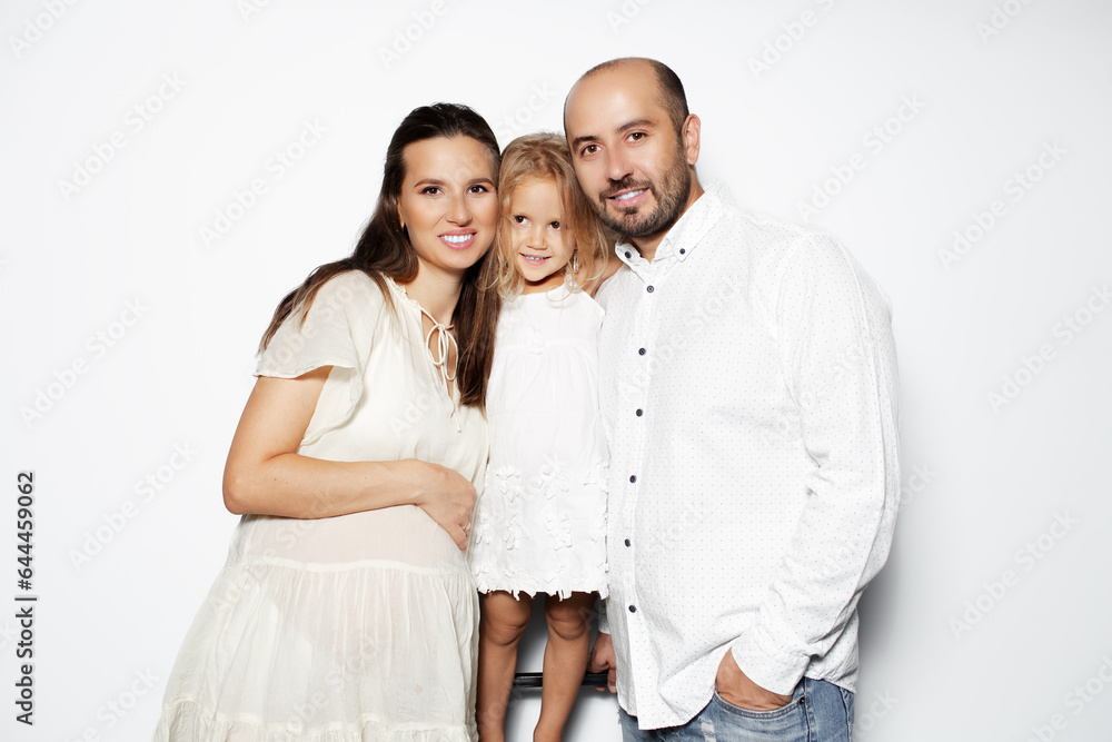 Studio portrait of happy family of three, pregnant mother, daughter and father, isolated on white background. Studio portrait of happy family of three, pregnant mother, daughter and father, isolated on white background.
