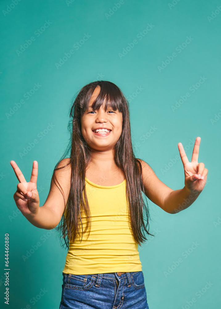 Happy ethnic girl child standing and showing victory sign against turquoise backdrop