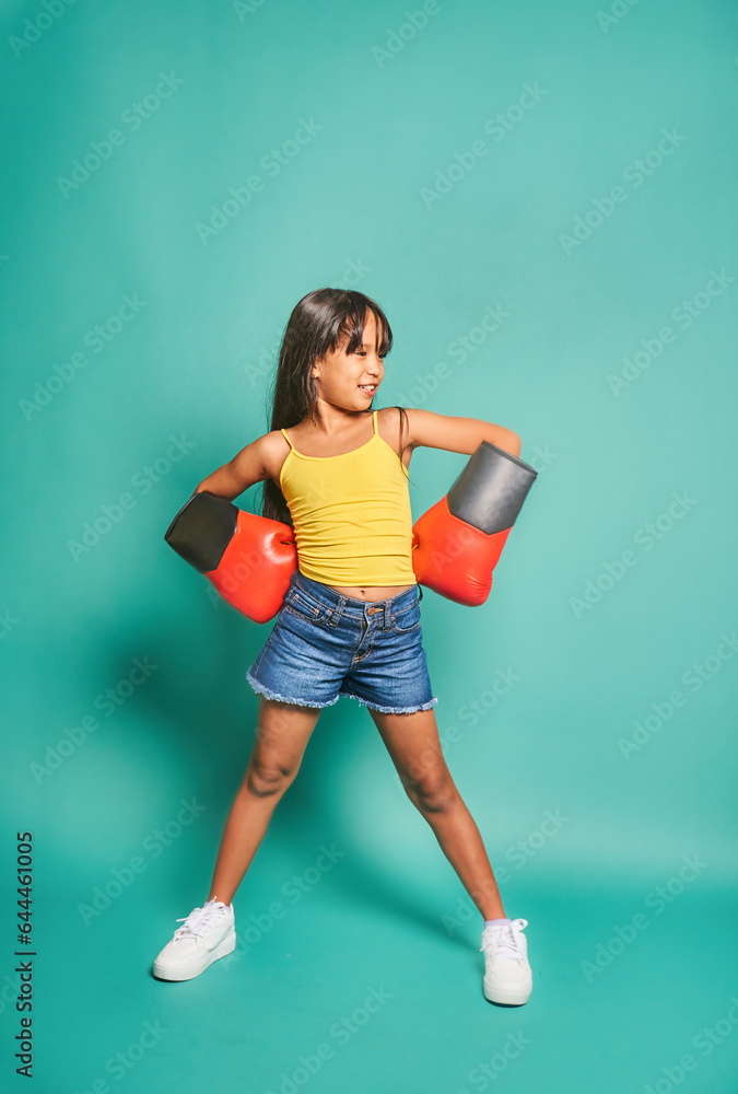 Cheerful ethnic kid girl in boxing gloves against turquoise background Cheerful ethnic kid girl in boxing gloves against turquoise background