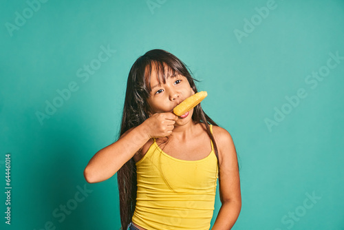 Happy ethnic girl child standing and eating ice cream in hand against turquoise backdrop photo