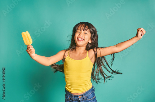 Happy ethnic girl child standing with popsicle in hand against turquoise backdrop