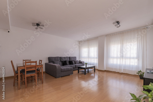 A living room with little furniture and a long gray sofa with a wooden floor and a large window