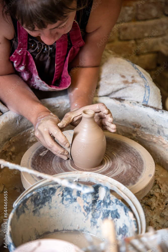 Une céramiste au travail dans une poterie artisanale.  Plan rapproché sur les mains et la technique de sculpture du vase 
