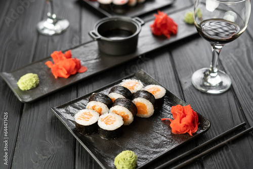 Maki rolls with salmon and cheese on black slate board with glass of wine in restaurant. Sushi menu. Japanese food.