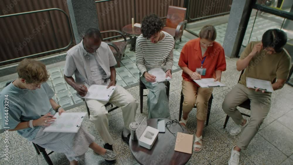 High angle shot of group of diverse people reading questions and writing on papers while having test during group therapy High angle shot of group of diverse people reading questions and writing on papers while having test during group therapy
