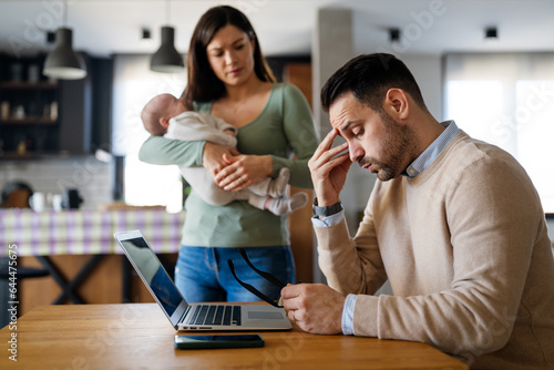 Father businessman try to work on laptop from home with wife and baby on background. photo