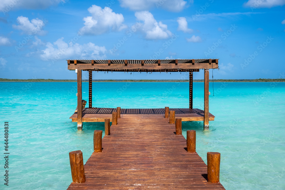 A wooden pier heading toward the horizon on a crystal clear blue water in Bacalar, Mexico