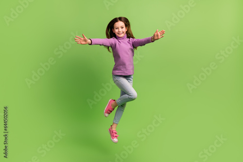 Full body cadre of funky schoolkid little girl jump active free time peaceful friendly greetings cuddles isolated on green color background