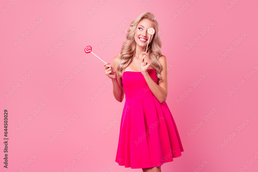 Photo of pretty lovely girl hold candy stick cover one eye look empty space isolated on pink color background Photo of pretty lovely girl hold candy stick cover one eye look empty space isolated on pink color background