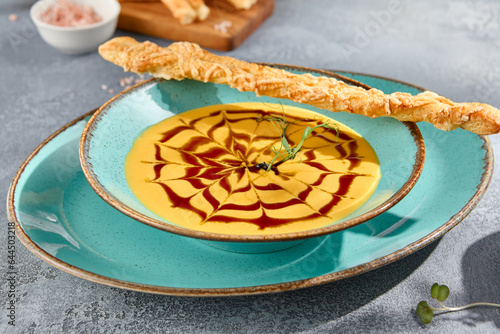 A closeup horizontal view of a bowl of creamy pumpkin soup with crostini. The texture of the soup and the gray concrete background create a feast for the eyes