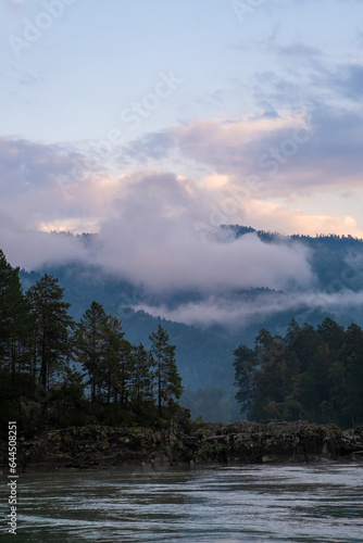 Mountains and peaks in fog at sunrise or sunset. Sun from behind the mountain. Amazing view of mountains and forest landscape with cloudy skies Altai mountains. Mountains and peaks in fog at sunrise © Анатолий Савицкий
