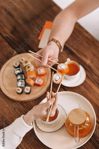 a woman and a man clink with Philadelphia rolls holding them with chopsticks over the table